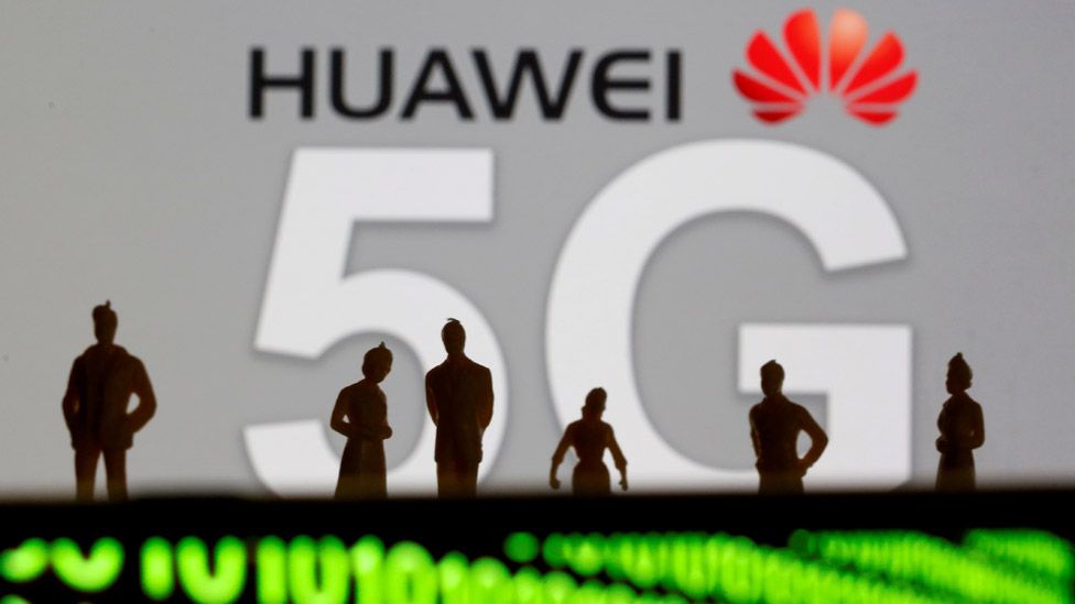 Small toy figures are seen in front of a displayed Huawei and 5G network logo