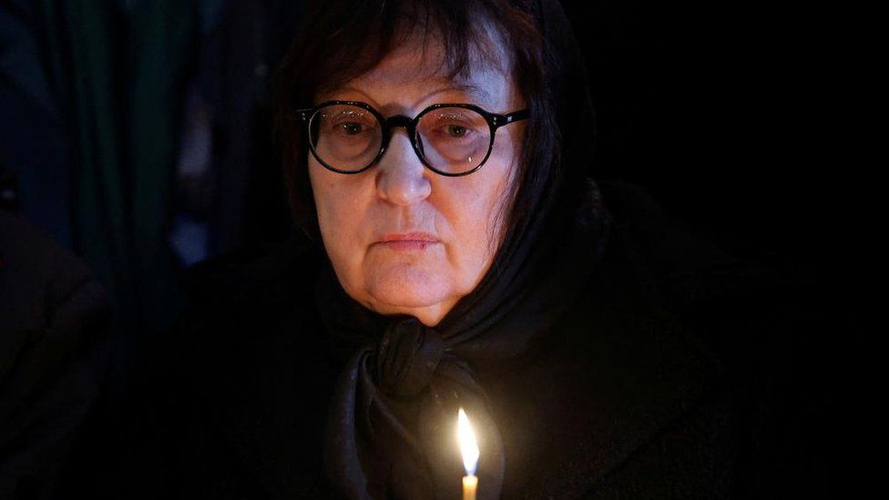 Lyudmila Navalnaya holds a candle, looking sad