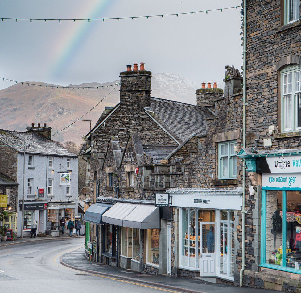 A view of shops in old stone buildings on a street with hills and a rainbow in the distance beyond