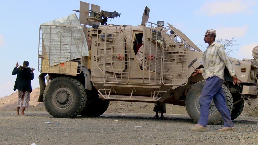 Pro-government militiamen walks past an armoured vehicle near the Yemeni city of Taiz