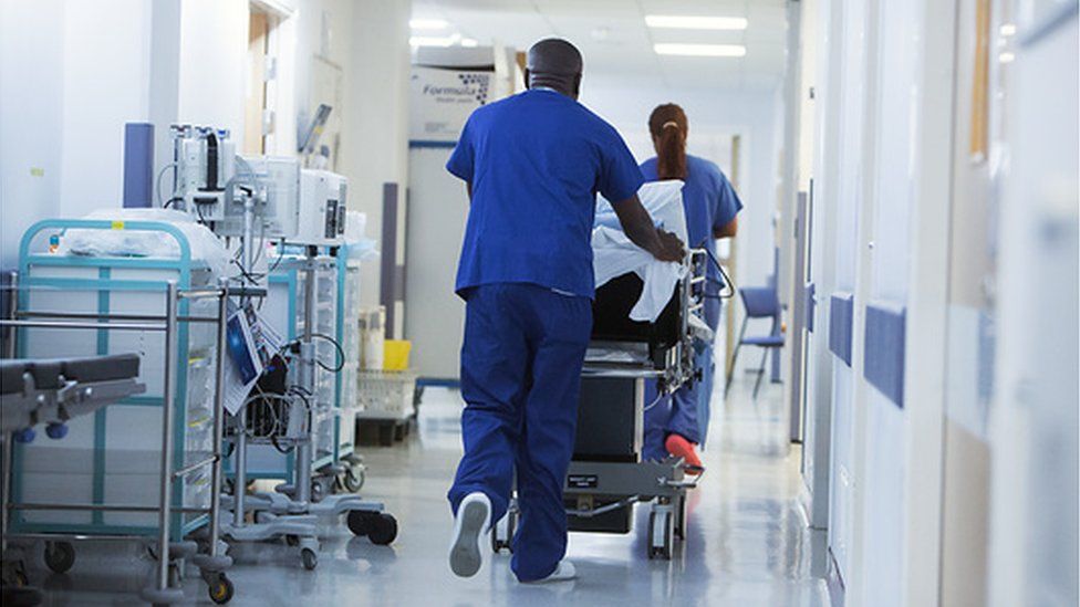 Patient in hospital trolley being pushed down a corridor