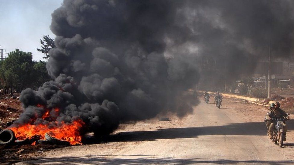 Rebel fighters from the Jaish al-Fatah (or Army of Conquest) brigades drive past burning tyres at an entrance to Aleppo, in the south-western frontline near the neighbourhood of Dahiyet al-Assad (03 November 2016)