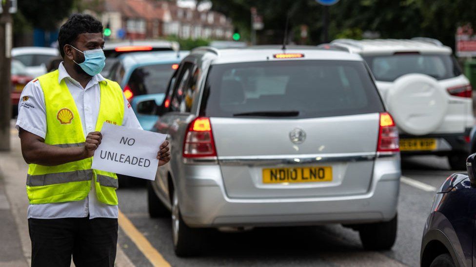 Сотрудник гаража Shell держит табличку на обочине дороги, информирующую участников дорожной очереди о том, что у них нет неэтилированного бензина, 25 сентября 2021 года в Блэкхите, Лондон, Великобритания.
