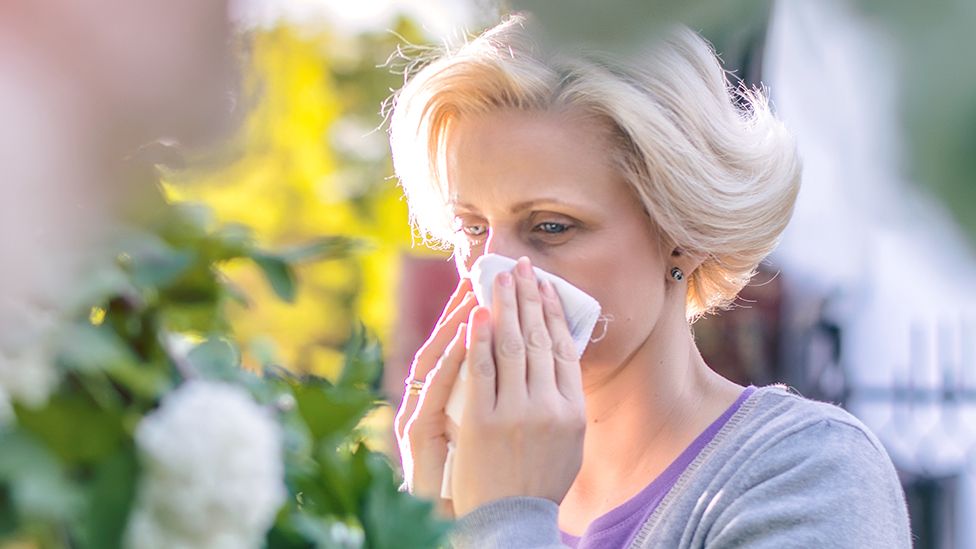 A person blows their nose in a garden