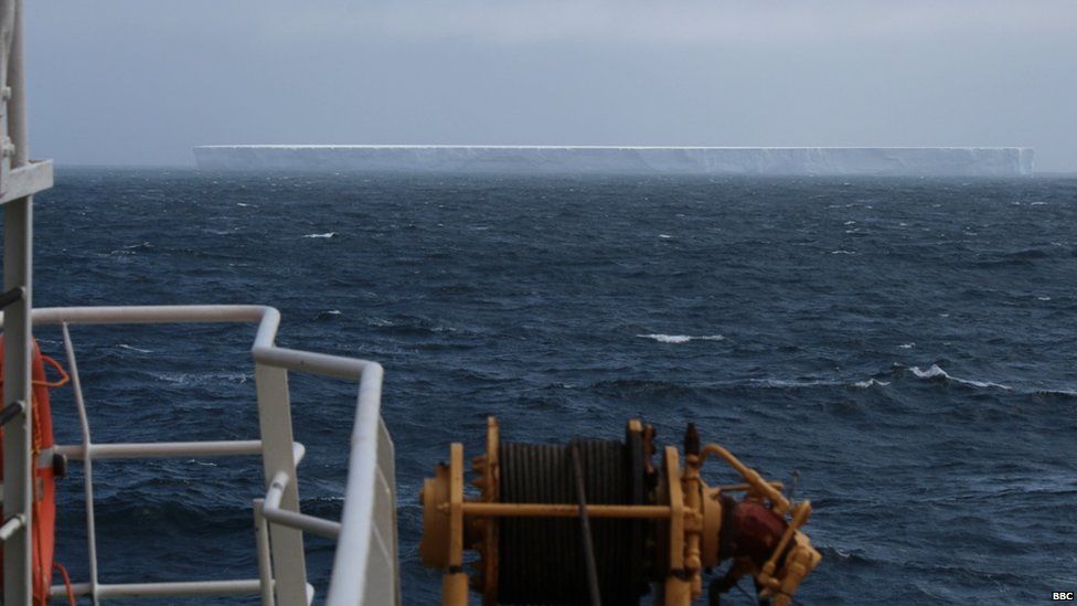 Large rectangular iceberg spotted in the middle of the ocean. The sky is grey.