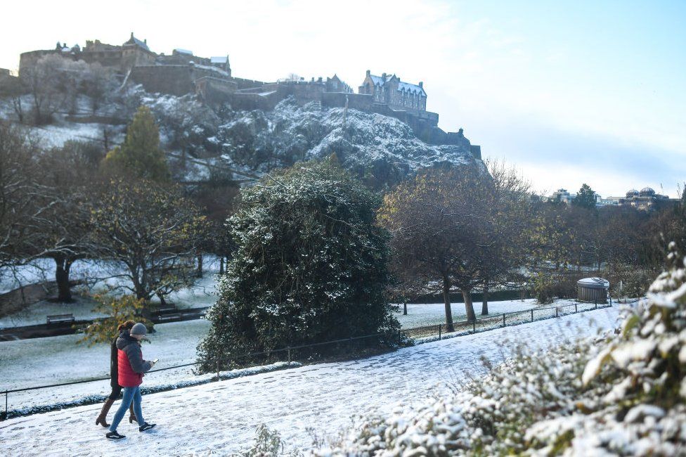 A couple walks along a snow covered path in front of Edinburgh Castle. A snow and ice warning from the Met Office remains in place after Storm Arwen brought high winds and heavy precipitation to north and eastern parts of the UK.
