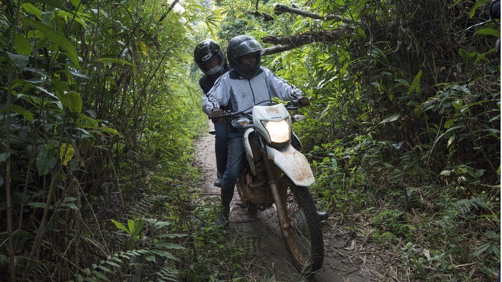 Health visitors travelling by motorbike through a remote area of DRC for a follow up meeting with a contact