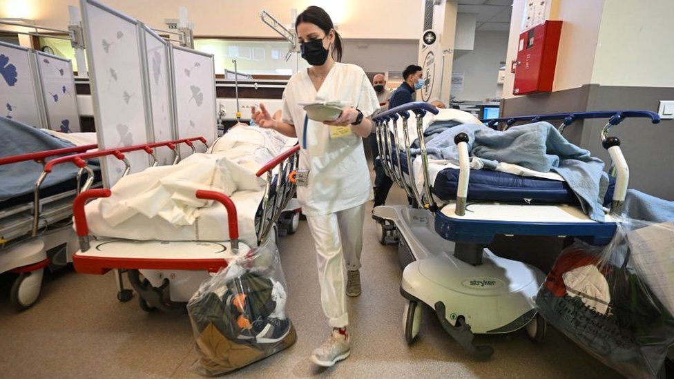 Медсестра проходит между кроватями двух пациентов в отделении неотложной помощи больницы Отпьер в Страсбурге, восточная Франция
