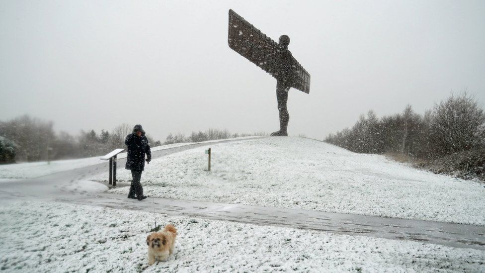 Man walks dog near Angel of the North in the snow