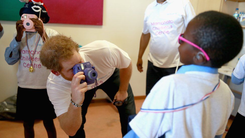 Prince Harry takes a photograph of a young boy at the new Mamohato Children's Centre in 2015