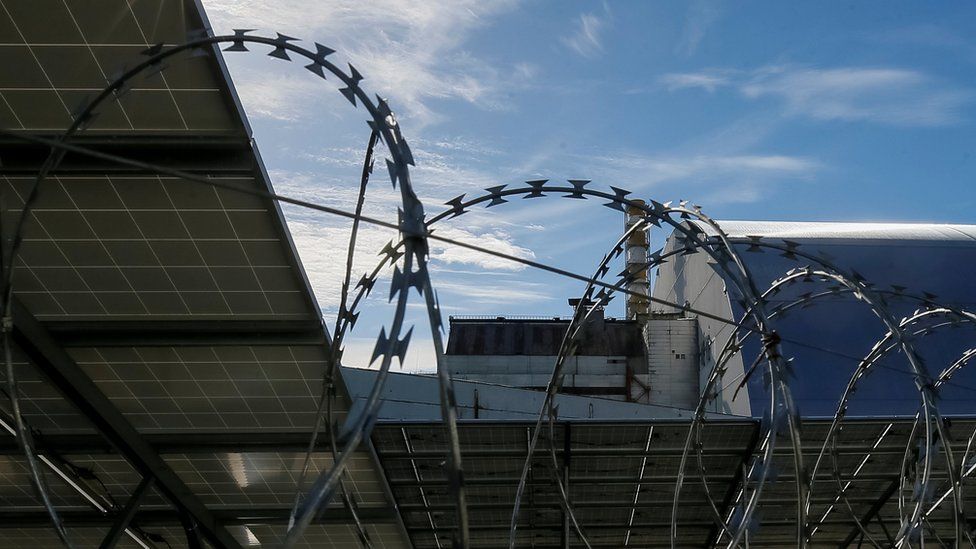 Solar panels are seen through barbed wire in front of the New Safe Confinement arch covering the damaged fourth reactor of the Chernobyl nuclear power plant in Ukraine on 5 October 2018