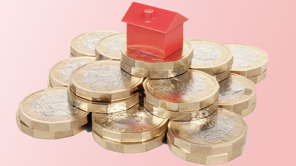 Miniature red house resting on a pile of pound coins.