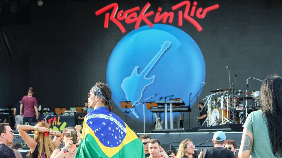 Man wrapped in Brazilian flag in front of a stage at Rock in Rio.