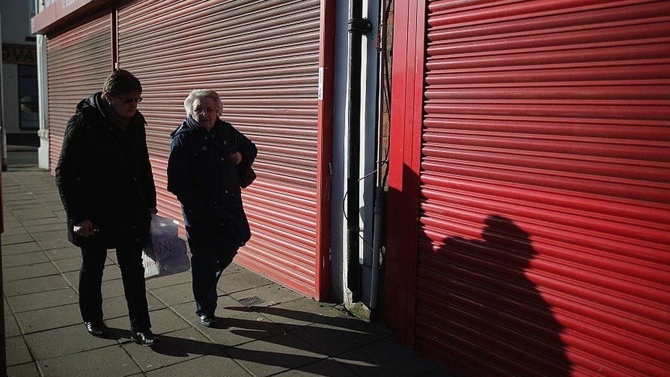 shoppers walk past shuttered unit