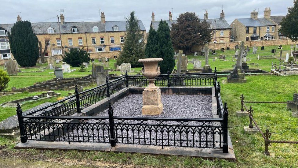Grave surrounded by newly-painted black railings and dominated by an urn that has lost its cracks