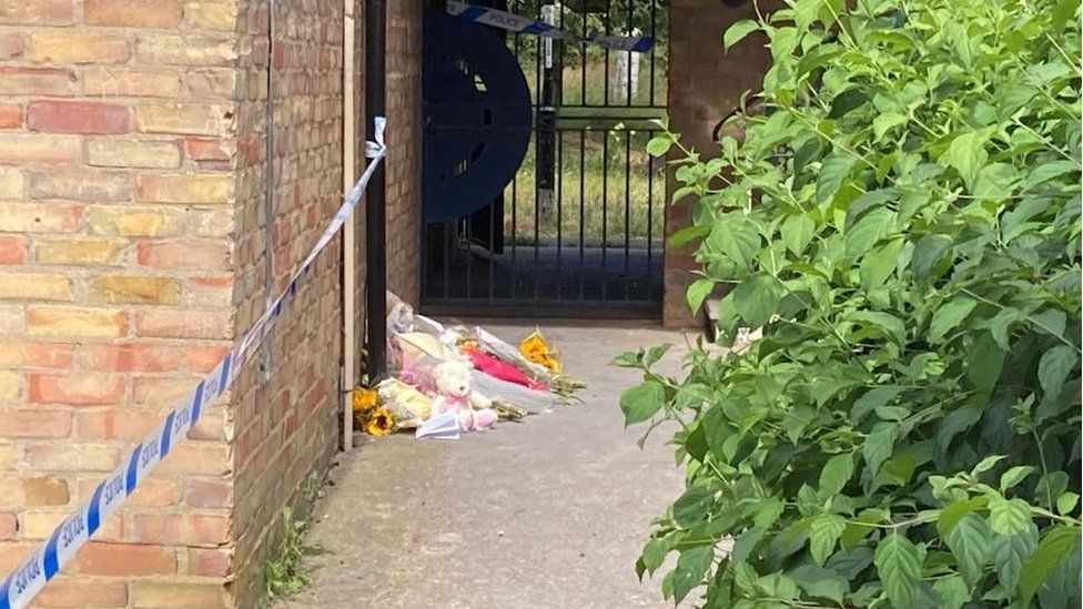 Police tape at the side of the building where soft toys and flowers have been left.