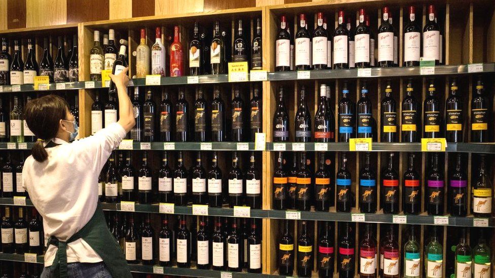 An employee works as Australian-made wine (on display shelves on R) are seen for sale at a store in Beijing on August 18, 2020.