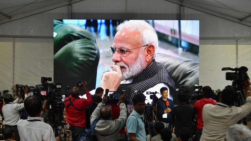Members of the media cover the development as India's Prime Minister Narendra Modi is seen on a tv screen as he watches the live broadcast of the soft landing of spacecraft Vikram Lander of Chandrayaan-2 on the surface of the Moon at ISRO Telemetry, Tracking and Command Network (ISTRAC) centre in Bangalore early on September 7, 2019.