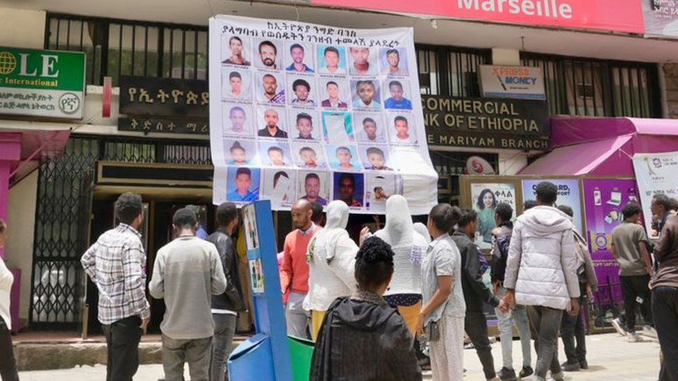 People examine a poster bearing the faces of customers the Commercial Bank of Ethiopia says haven't returned money the bank lost during a glitch