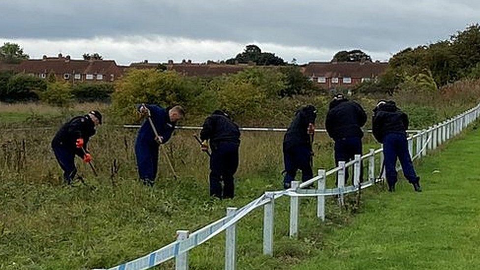 Police officers search for evidence in shrubs