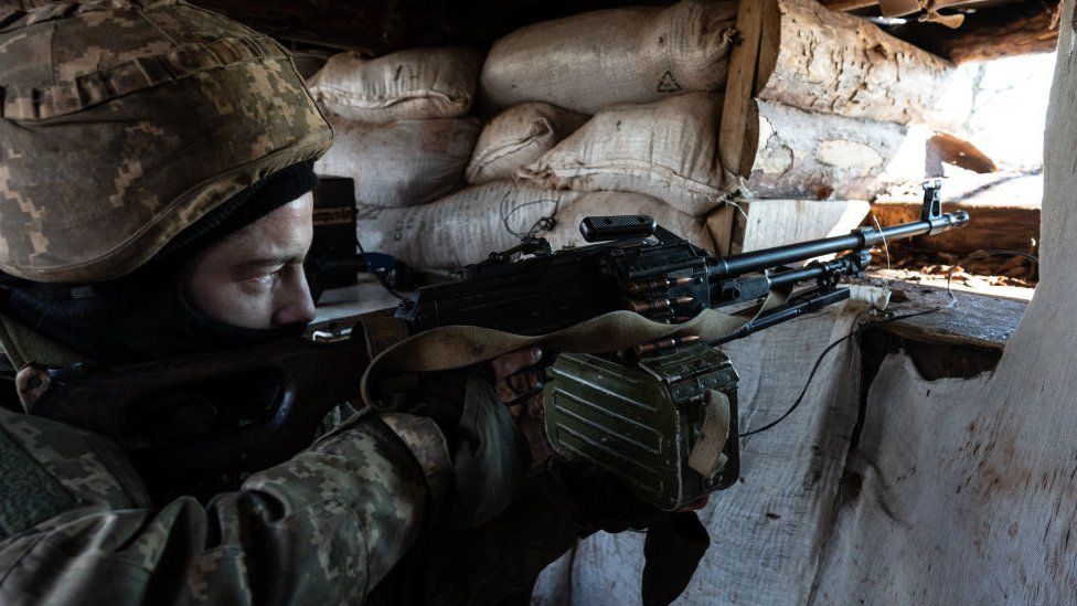 A Ukrainian serviceman points a machine gun through an opening in a sandbag bunker during military exercises