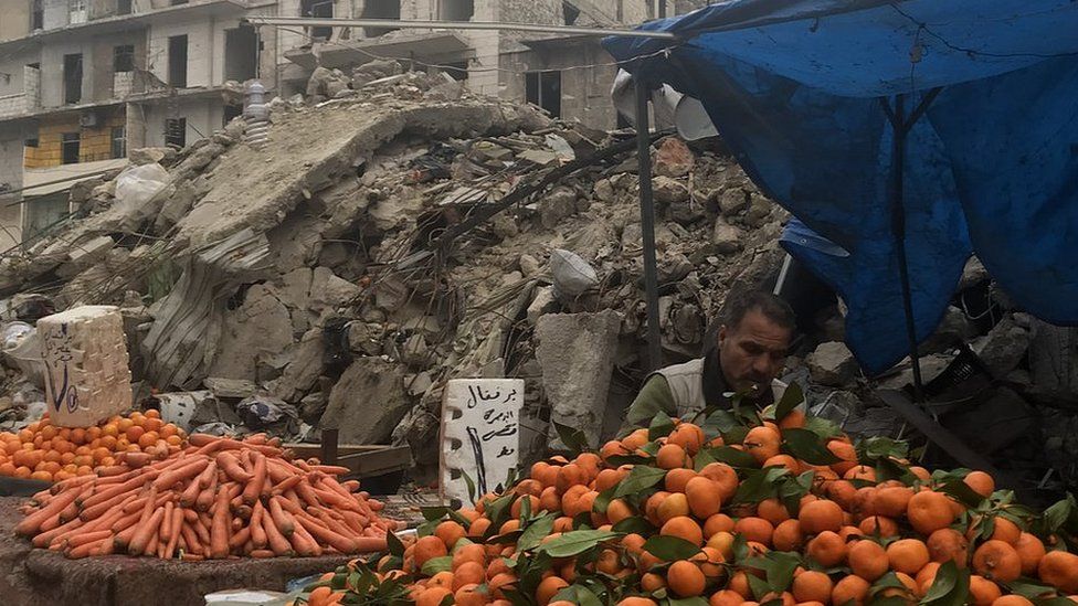 A man pictured at a market stall in Aleppo surrounded by rubble