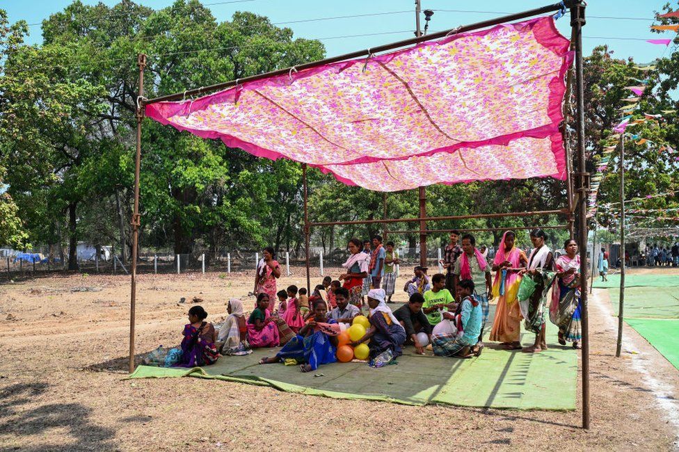 Voters take shelter from the sun, outside a polling station to cast their ballot on a hot day during the first phase of voting for the India's general election, in Dugeli village of Dantewada district of Chhattisgarh state on April 19, 2024.
