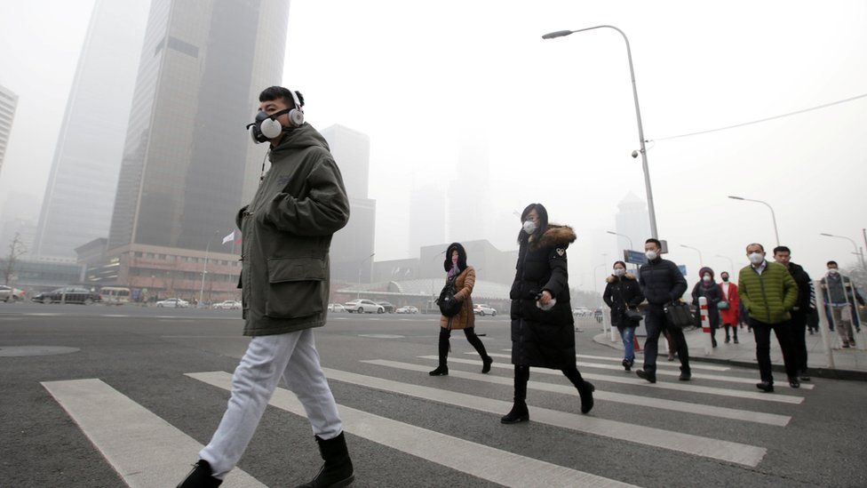 People in face masks walk through a smoggy Beijing street