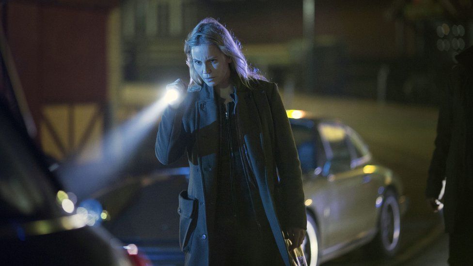 Saga in a still from The Bridge, at night holding a torch