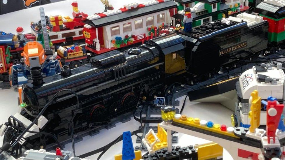 Black steam train in Lego, alongside a railway track with another locomotive