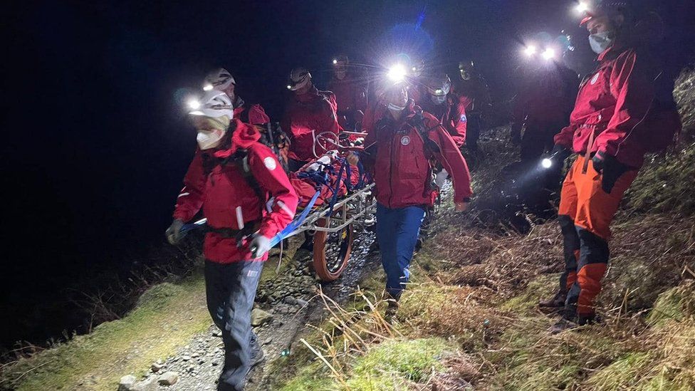 Volunteers stretcher a woman off a mountain in the dark