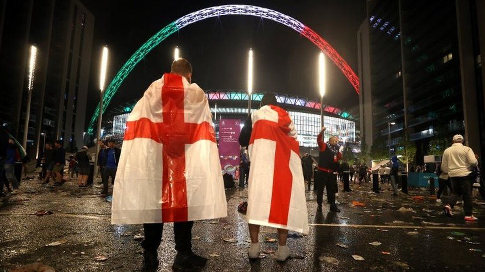 England fans draped in national flags leave Wembley stadium in London. Photo: 11 July 2021