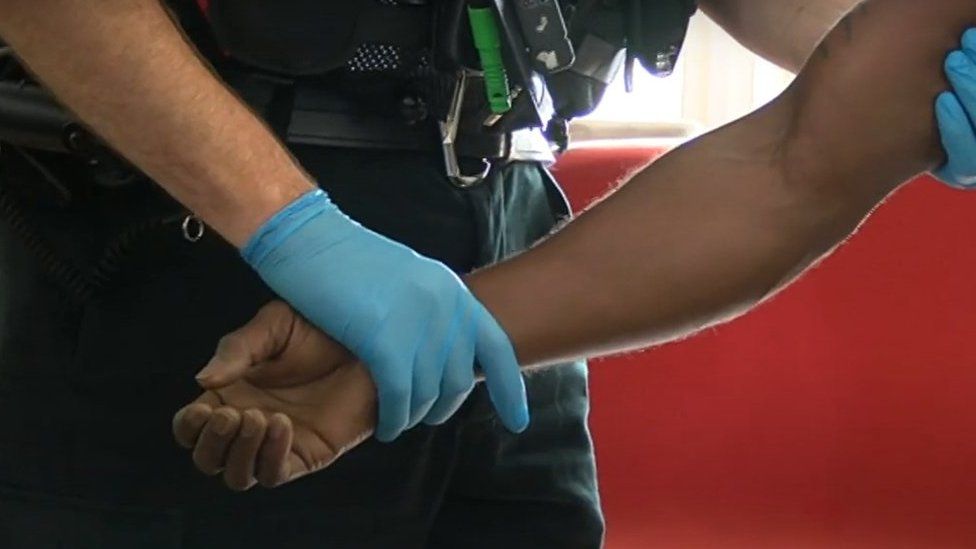 Close-up of suspect's arm being held by a police officer wearing blue latex gloves
