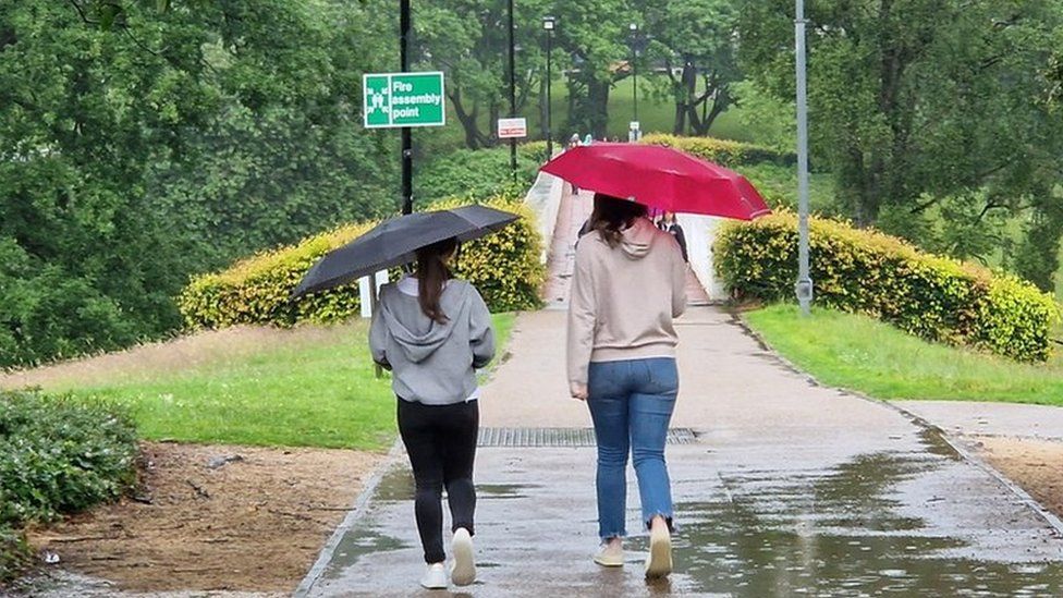 Two young women walk along a pathway holding up umbrellas