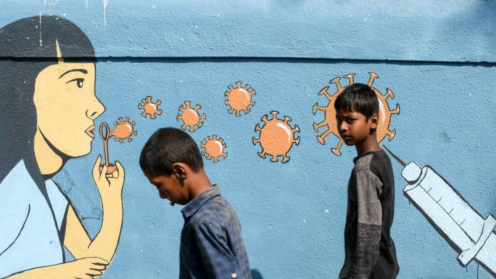 Boys walk past a painted graffiti to create awareness about coronavirus. Due to the spike of coronavirus cases in Maharashtra state, people have been advised to maintain social distance, wear masks and sanitize hands regularly.