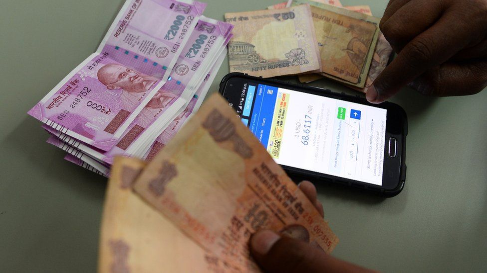 An Indian man checks the currency exchange rate on a mobile phone in New Delhi on November 24, 2016. India's rupee headed towards a record low against the dollar November 24, weakened by the government's shock currency shake-up and a greenback surge on expectations of a rate hike next month.
