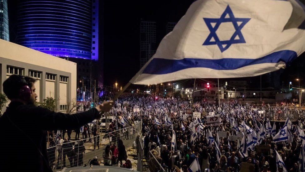 Протестующий размахивает израильским флагом во время массовой акции протеста против правительственного плана пересмотра судебной системы 11 марта 2023 года в Тель-Авиве