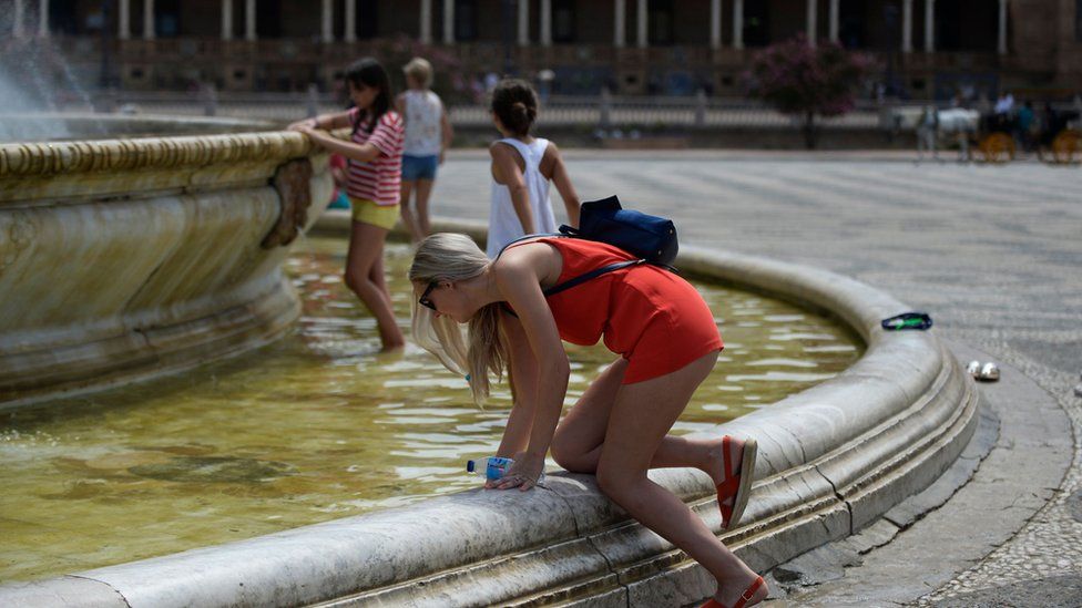 A woman refreshes herself in a fountain at Plaza de Espana, on a hot summer day in Sevilla
