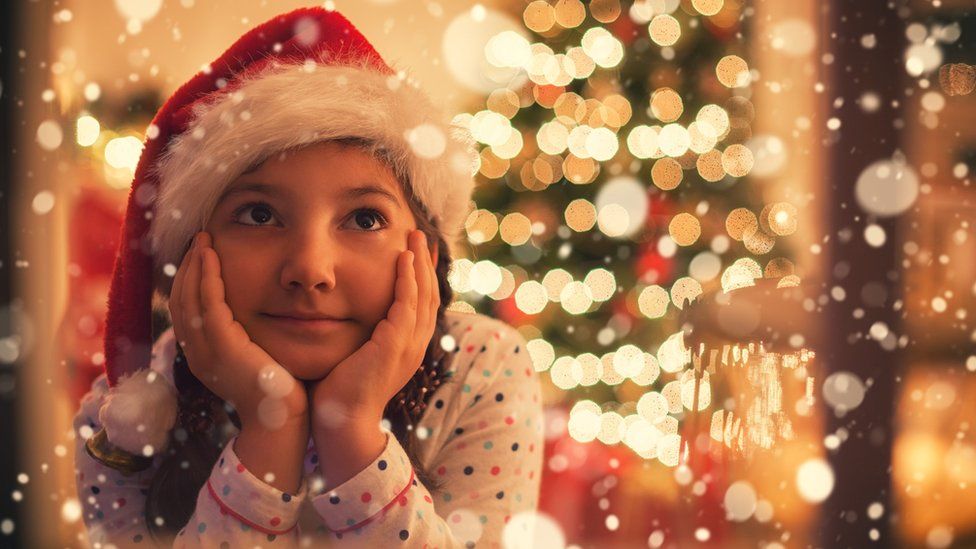 Christmas Eve,little girl with Santa hat sitting in living room in warm holiday atmosphere and she looking through window,while waiting for Santa