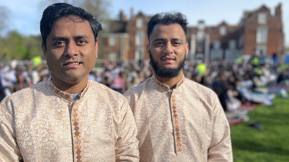 Two Bangladeshi men in Muslim dress stand in front of crowds outside
