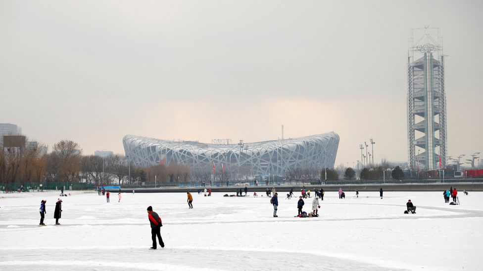Люди катаются на коньках по замерзшему каналу перед национальным стадионом «Птичье гнездо» в Пекине, январь 2022 года