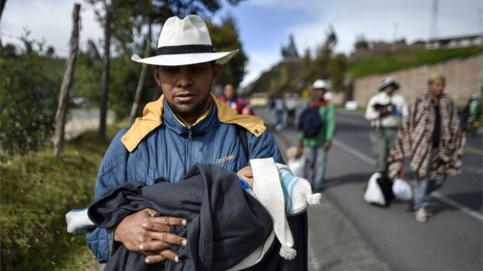 Мужчина из Венесуэлы несет своего ребенка, пока идет по Панамериканскому шоссе в Колумбии по пути в Перу