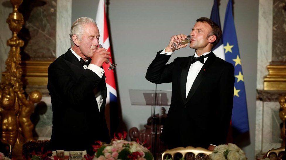 King Charles III and French President Emmanuel Macron drink from glasses at a state banquet at the Palace of Versailles