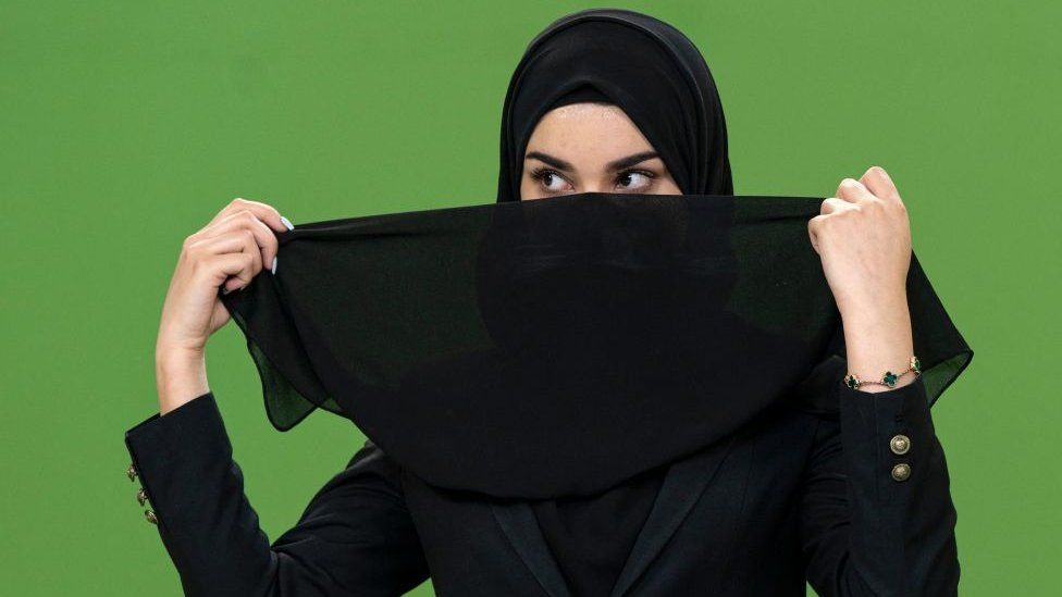 An Afghan female presenter for 1TV channel, Masheed Barzz, prepares to cover her face by a veil before a live broadcast at 1TV channel station in Kabul on May 25, 2022.