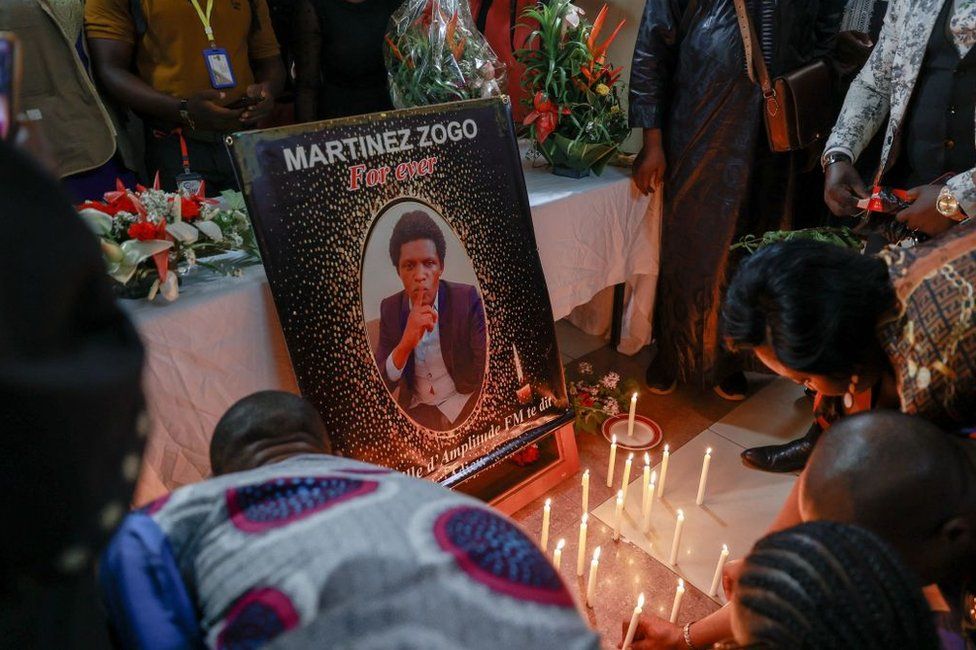 Candles and tributes are laid out in front of a poster of Martinez Zogo,