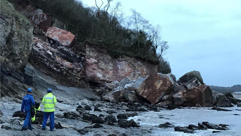 Two men standing in front of the rock fall on Oxwich Bay