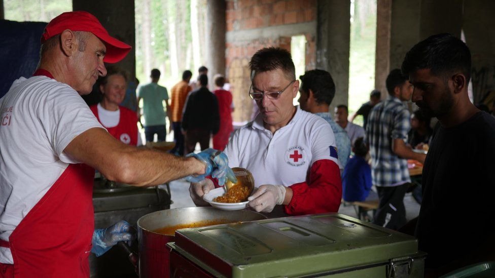 A man in a red cap and apron serves a medical worker and resident alike at the makeshift accommodations