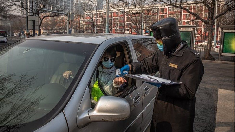 A security guard wearing a protective face mask checks body temperature of a driver at the entrance to a parking at residential area of Sanlitun in Beijing, China, 11 February 2020.