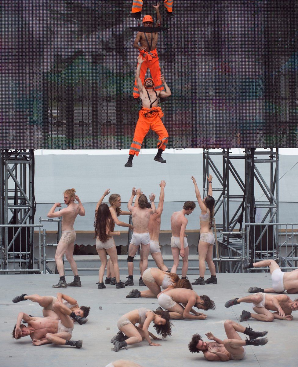 Artists in underwear roll on floor as others dressed as construction workers are lifted into the sky - at opening ceremony of the Gotthard rail tunnel, the longest tunnel in the world