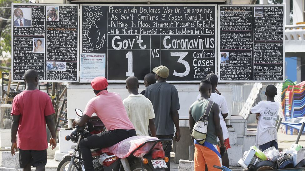 People reading a blackboard news board in Monrovia, Liberia - Monday 30 March 2020